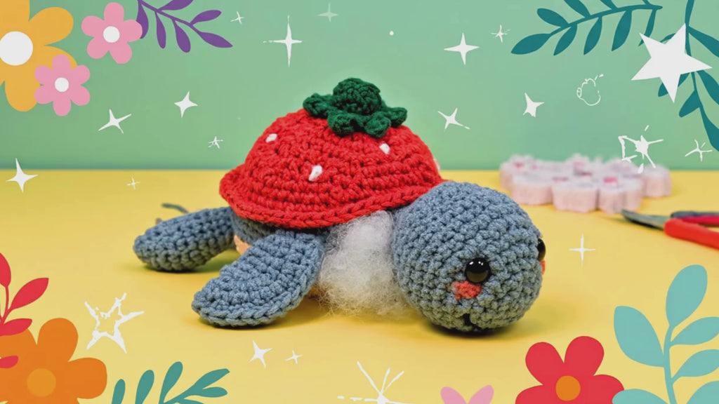 Handmade crochet strawberry turtle plushie in blue with coral strawberry shell and green leaves on warm background with Cozimyco Ready text